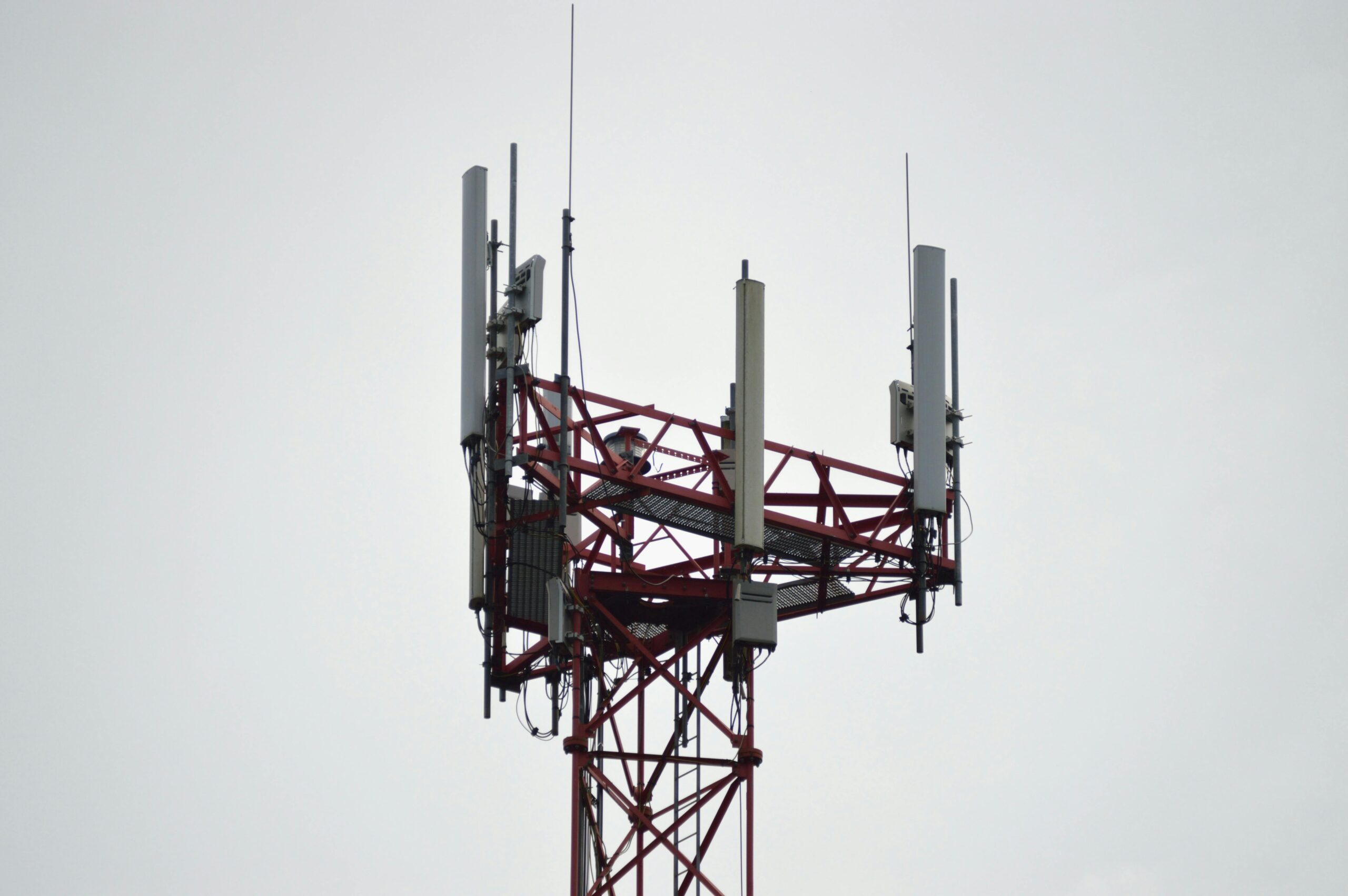 Cell tower antenna array with multiple directional panels and cabling against a grey sky, illustrating hybrid DAS and booster integration