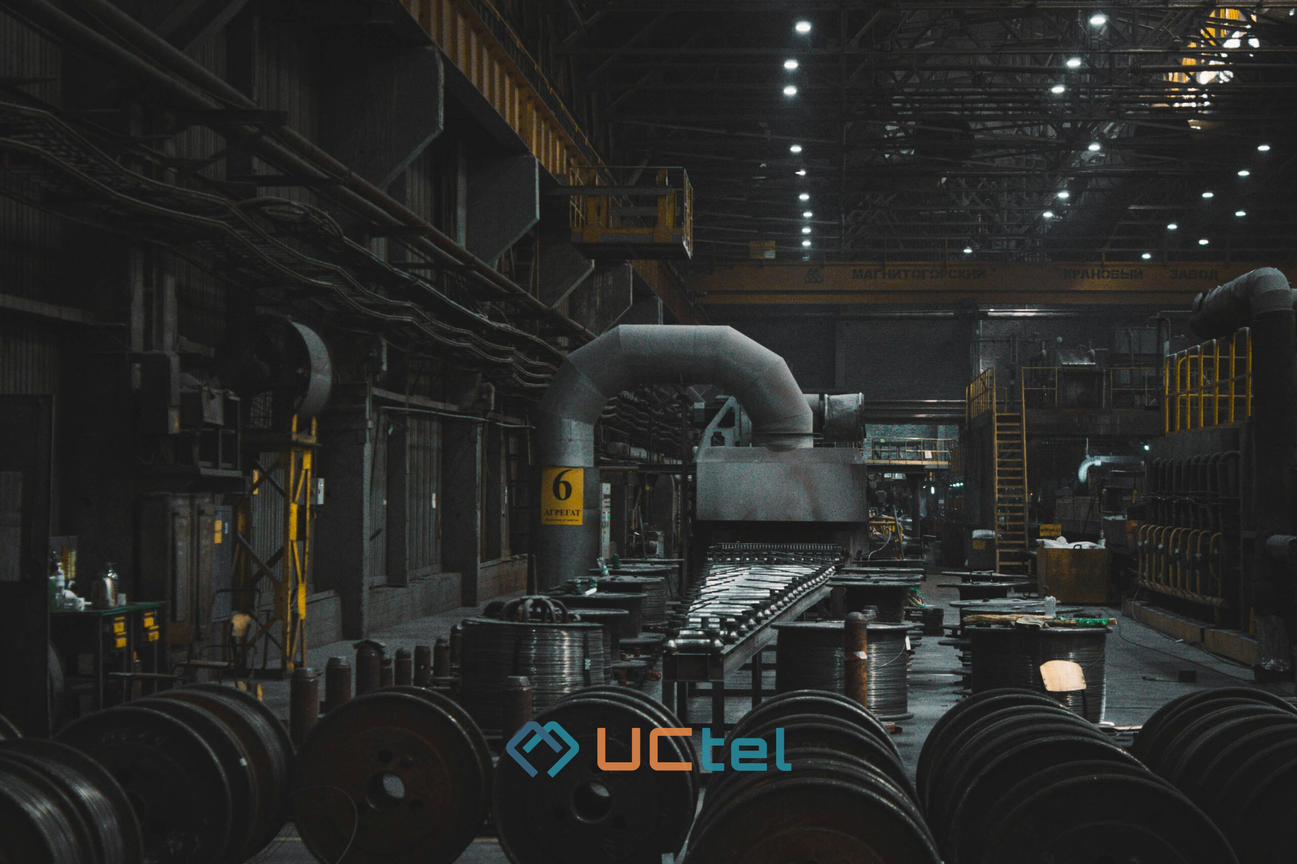 Dark industrial factory interior with heavy machinery and steel coils, illustrating signal booster monitoring in harsh environments